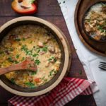 Eintopf in einem Topf mit Holzlöffel, dekoriert mit Petersilie. Serviert auf Reis in Schale. Paprika und Tuch daneben.