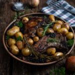 Gegrillte Lammkoteletts mit rosig gebratenen Kartoffeln und Rosmarin auf einem Holztisch, rustikal serviert.