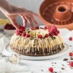 Hand dekoriert Kranzkuchen mit Himbeeren und weißer Schokolade; Gugelhupfform im Hintergrund.