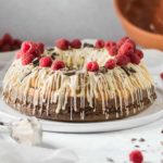 Gugelhupf mit weißer Schokolade, Himbeeren und Schokoladenstücken garniert auf einem Teller.