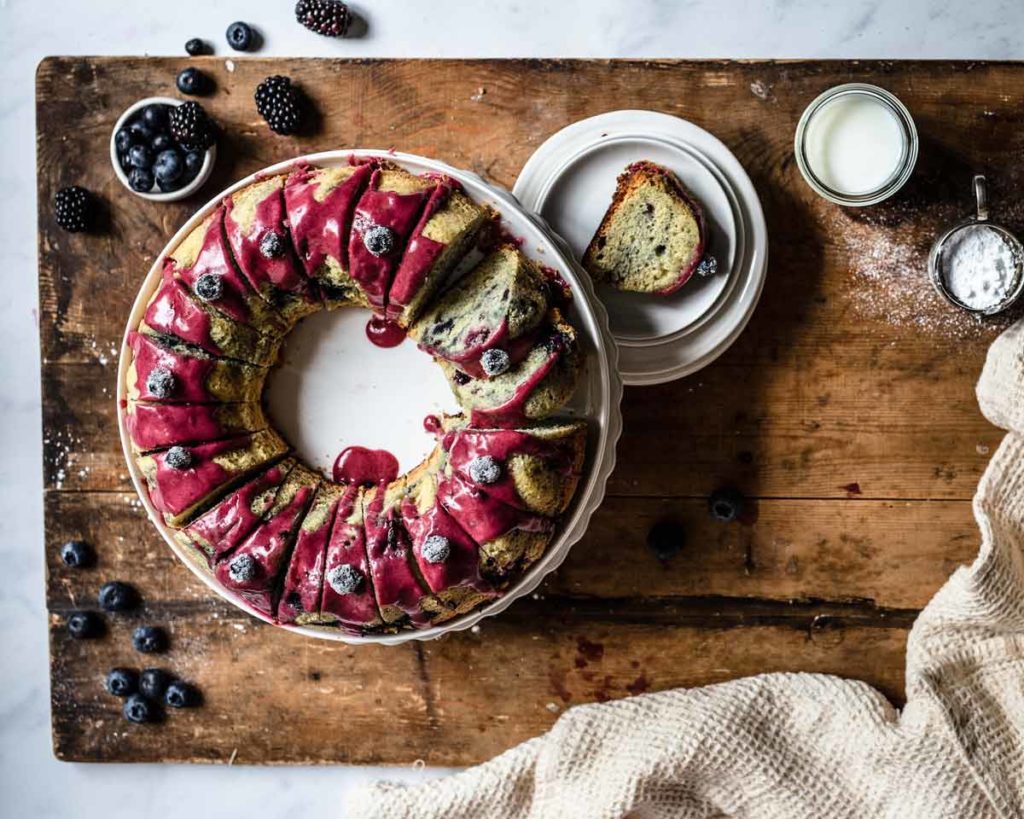 Gugelhupf mit Beeren und roter Glasur auf rustikalem Holztisch, serviert mit Milch und Puderzucker.