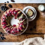 Gugelhupf mit Beeren und roter Glasur auf rustikalem Holztisch, serviert mit Milch und Puderzucker.