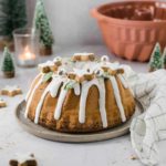 Weihnachtlicher Gugelhupf mit Zuckerguss, Plätzchen und Winterdeko auf einem Tisch mit Kerze und Tannenbäumchen.
