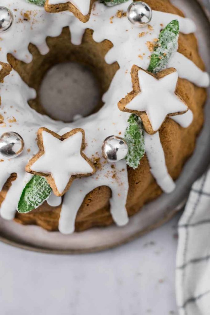 Weihnachtskranzkuchen mit Zuckerguss, sternförmigem Gebäck, silbernen Kugeln und grüner Dekoration.