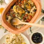 Terrakottaform mit gebackenem Huhn, Tomaten, Zitrone, Oliven und Reis. Daneben ein Teller mit einer Portion.