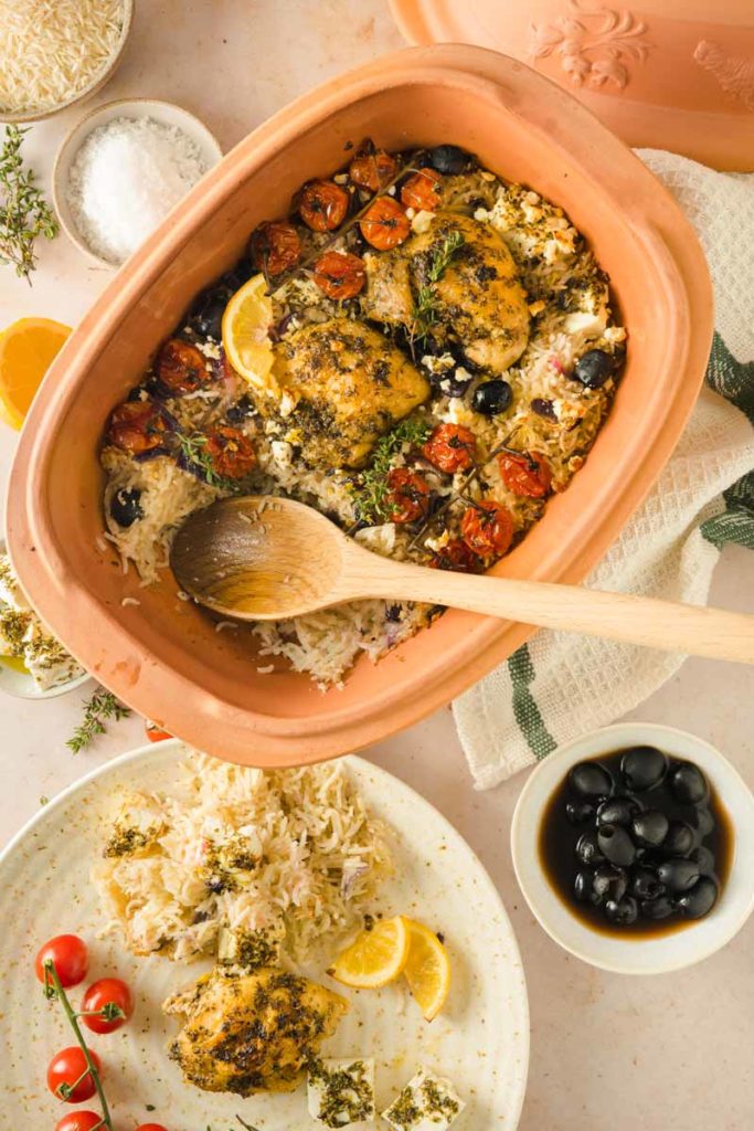 Terrakottaform mit gebackenem Huhn, Tomaten, Zitrone, Oliven und Reis. Daneben ein Teller mit einer Portion.