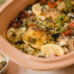 Mediterranes Ofengericht mit Hühnchen, Reis, Kirschtomaten, Feta und Zitronenscheiben in einer Keramikform.