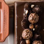 Schokoladenkuchen mit Haselnuss-Pralinen und Schokocreme dekoriert. Links ein Römertopf.