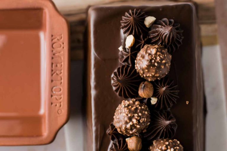 Schokoladenkuchen mit Haselnuss-Pralinen und Schokocreme dekoriert. Links ein Römertopf.