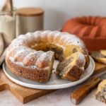 Marmor-Gugelhupf mit Puderzucker bestäubt auf weißem Teller, angeschnitten, daneben Backform und Zutaten.