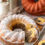 Saftiger Marmorkuchen mit Puderzucker bestäubt, serviert auf einem Teller, mit angeschnittenem Stück und Silikonform im Hintergrund.