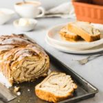 Gezopfter Kuchen mit Zuckerglasur auf einem Blech, daneben Tassen und Tellerstücke auf einem Tisch.