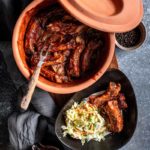 Römertopf mit marinierten Rippchen, serviert mit Krautsalat und Soße, auf einem rustikalen Tisch gedeckt.