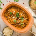 Hühnchen-Tajine mit Mandeln und Granatapfelkernen in Keramikform, serviert mit Couscous, frischen Kräutern und Aprikosen.