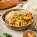 Schale mit Couscous und marokkanischem Eintopf, garniert mit Koriander. Daneben getrocknete Aprikosen in einer kleinen Schale.