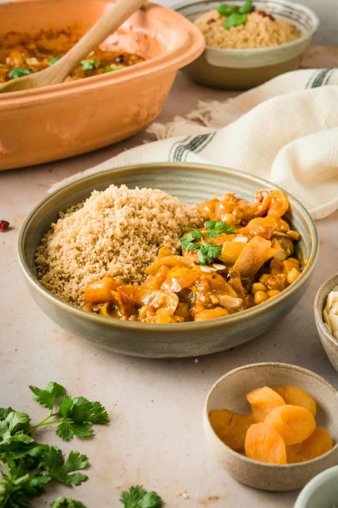 Schale mit Couscous und marokkanischem Eintopf, garniert mit Koriander. Daneben getrocknete Aprikosen in einer kleinen Schale.