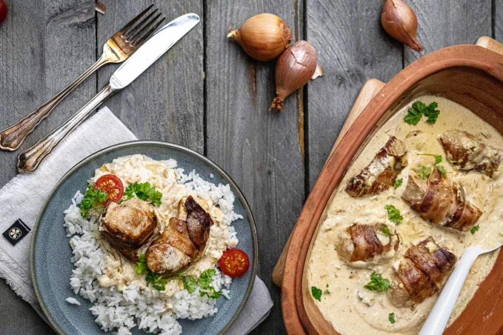 Gericht mit gefüllten Fleischröllchen in Rahmsauce, serviert mit Reis und Tomaten, dekoriert mit Petersilie.