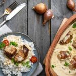 Gericht mit gefüllten Fleischröllchen in Rahmsauce, serviert mit Reis und Tomaten, dekoriert mit Petersilie.