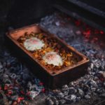 Zweieier-Topf auf offenem Feuer im Tontopf, umgeben von glühenden Kohlen, wird gekocht.