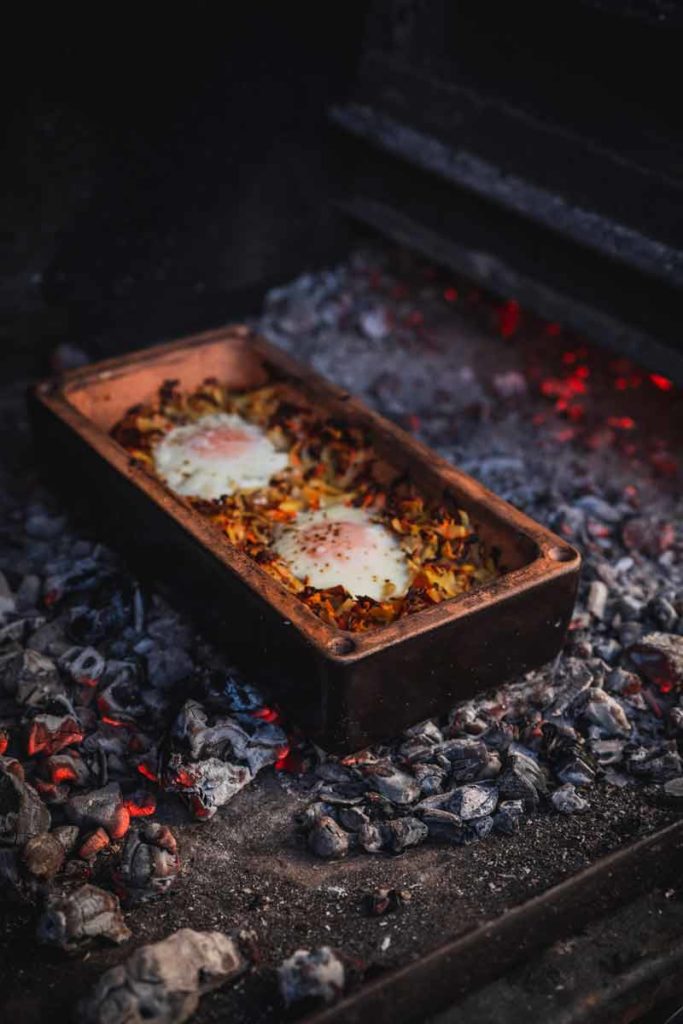 Zweieier-Topf auf offenem Feuer im Tontopf, umgeben von glühenden Kohlen, wird gekocht.