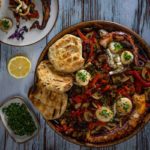 Gegrillter Pulpo mit Brot und Gemüse auf einem Teller, Zitrone und Kräuter auf Holztisch.