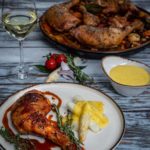 Gegrilltes Hähnchen mit Spargel und Sauce, neben einem Glas Weißwein und tomatendekoriertem Rosmarin.