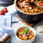 Orecchiette mit Tomaten, Paprika und Käse in einem schwarzen Topf serviert, frische Basilikumblätter, daneben Gewürzmühle.