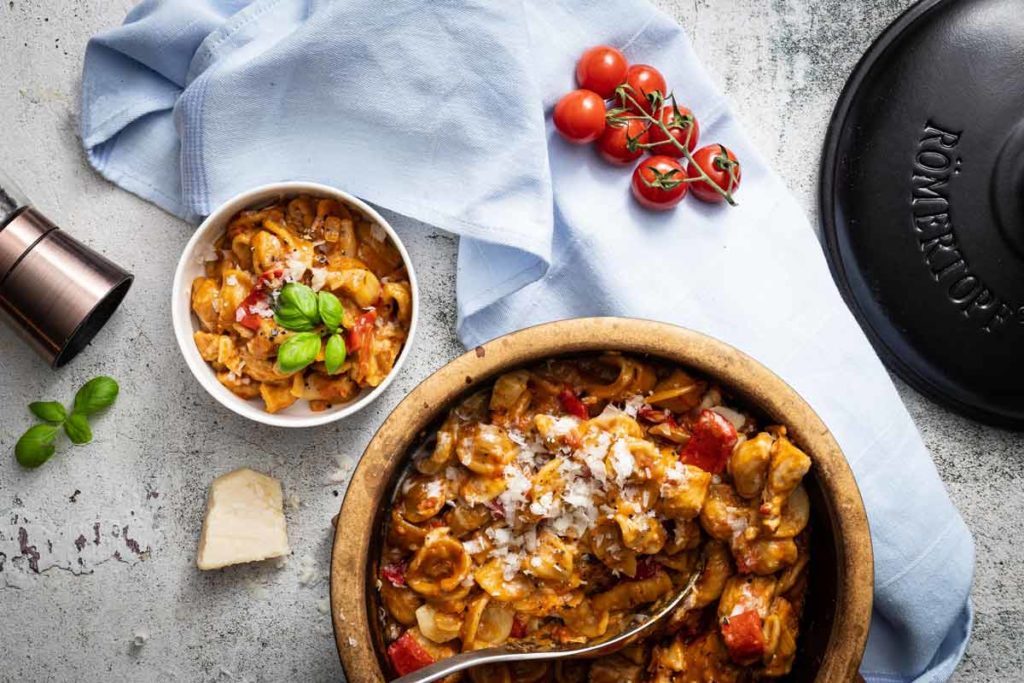 Schüssel mit cremigen Nudeln, dekoriert mit Basilikum. Daneben Kirschtomaten und ein Stück Parmesan auf einer Tischdecke.