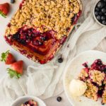 Obst-Crumble mit knuspriger Streuselkruste, serviert mit Vanilleeis; frische Beeren als Dekoration.