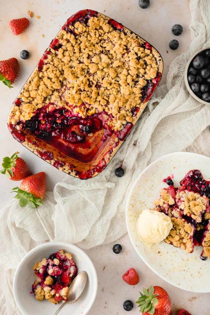 Obst-Crumble mit knuspriger Streuselkruste, serviert mit Vanilleeis; frische Beeren als Dekoration.