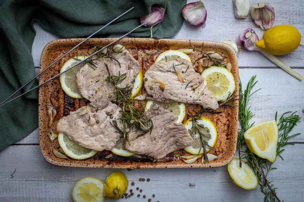 Gebratenes Fleisch auf Zitronenscheiben mit Rosmarin und Knoblauch, angerichtet in einer rechteckigen Pfanne.