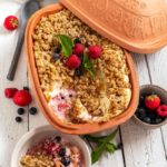 Lehm-Backform mit Haferauflauf und Beeren, darunter eine Portion in einer Schale. Deko mit frischen Beeren und Minze.