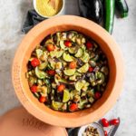 Gemüse-Ratatouille in einem Römertopf mit Zucchini, Auberginen, Tomaten und Pinienkernen, daneben Hirse und ganze Gemüsesorten.