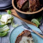 Römertopf mit Hackbraten und Blumenkohl im Anschnitt, serviert auf einem Teller mit Besteck.