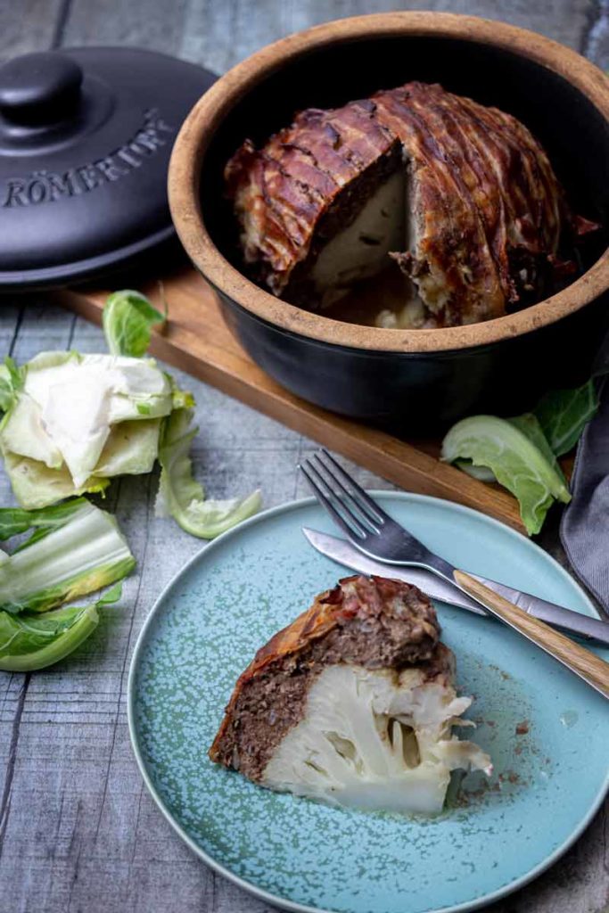Römertopf mit Hackbraten und Blumenkohl im Anschnitt, serviert auf einem Teller mit Besteck.