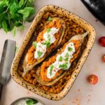 Gefüllte Auberginen mit roten Linsen, Joghurt und Kräutern in einer Auflaufform, dekoriert mit Tomaten und frischen Kräutern.