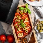 Ofenform mit Kichererbsen, Tomaten, Feta, Oliven und Basilikum. Daneben Tomaten und eine Schüssel mit Oliven.