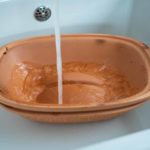 Terrakotta-Backform wird unter laufendem Wasser in einem weißen Waschbecken gereinigt.