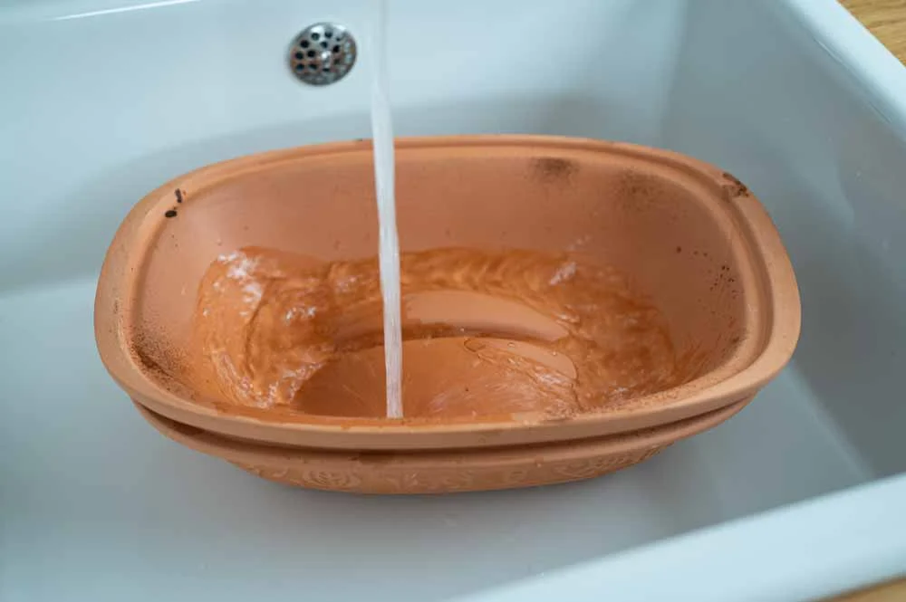 Terrakotta-Backform wird unter laufendem Wasser in einem weißen Waschbecken gereinigt.