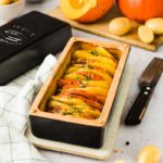 Herbstliches Gratin mit Kürbis und Kartoffeln in einer Auflaufform, umgeben von Kürbishälften und Kartoffeln.