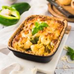 Überbackene Pasta mit Gemüse und Käse in einer Auflaufform, dekoriert mit Basilikum, neben Paprika und Zwiebel.