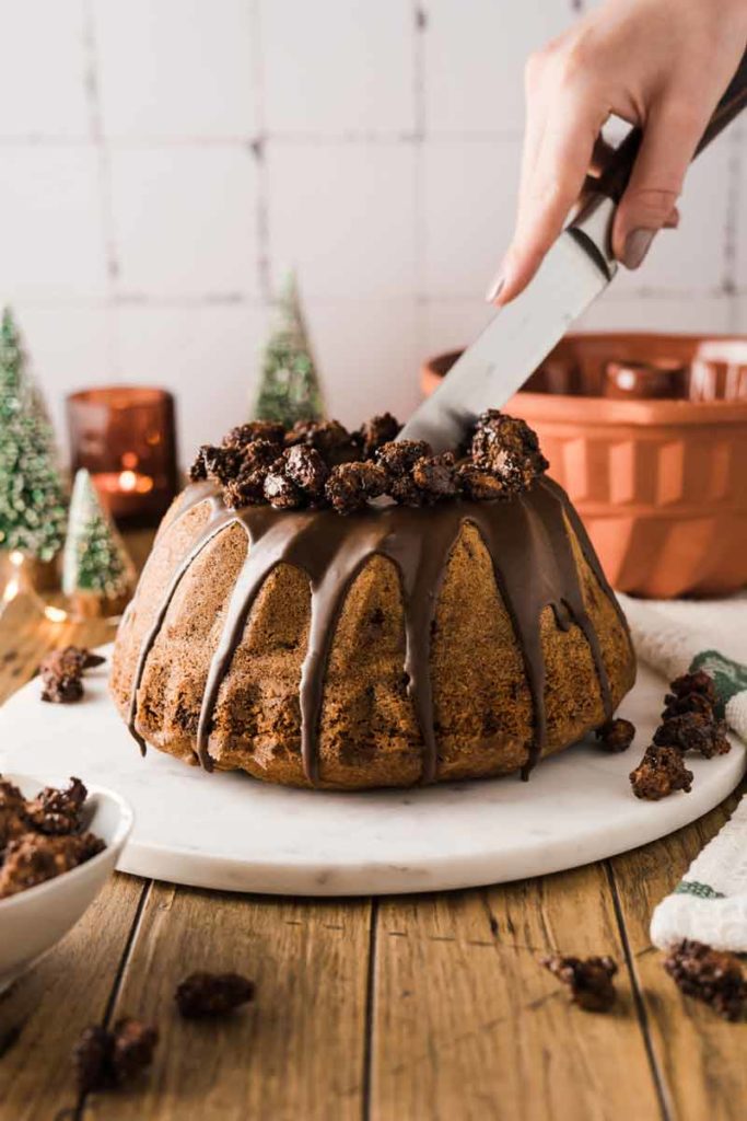 Person schneidet Schokoladenkuchen auf Marmorplatte an, dekoriert mit Krümeln, festliche Atmosphäre.