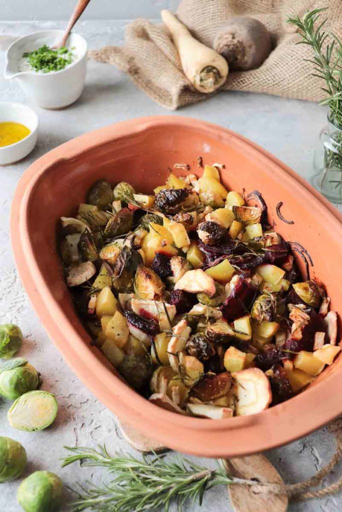 Gebratene Gemüse in einer Terrakottaschale, umgeben von frischen Kräutern und Gewürzen auf einem Steintisch.