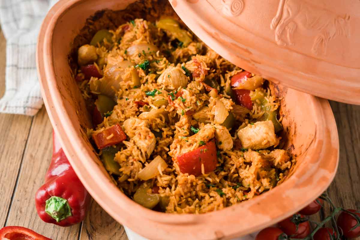 Reisgericht mit Hühnchen und Paprika in einem römischen Schmortopf auf Holztisch.