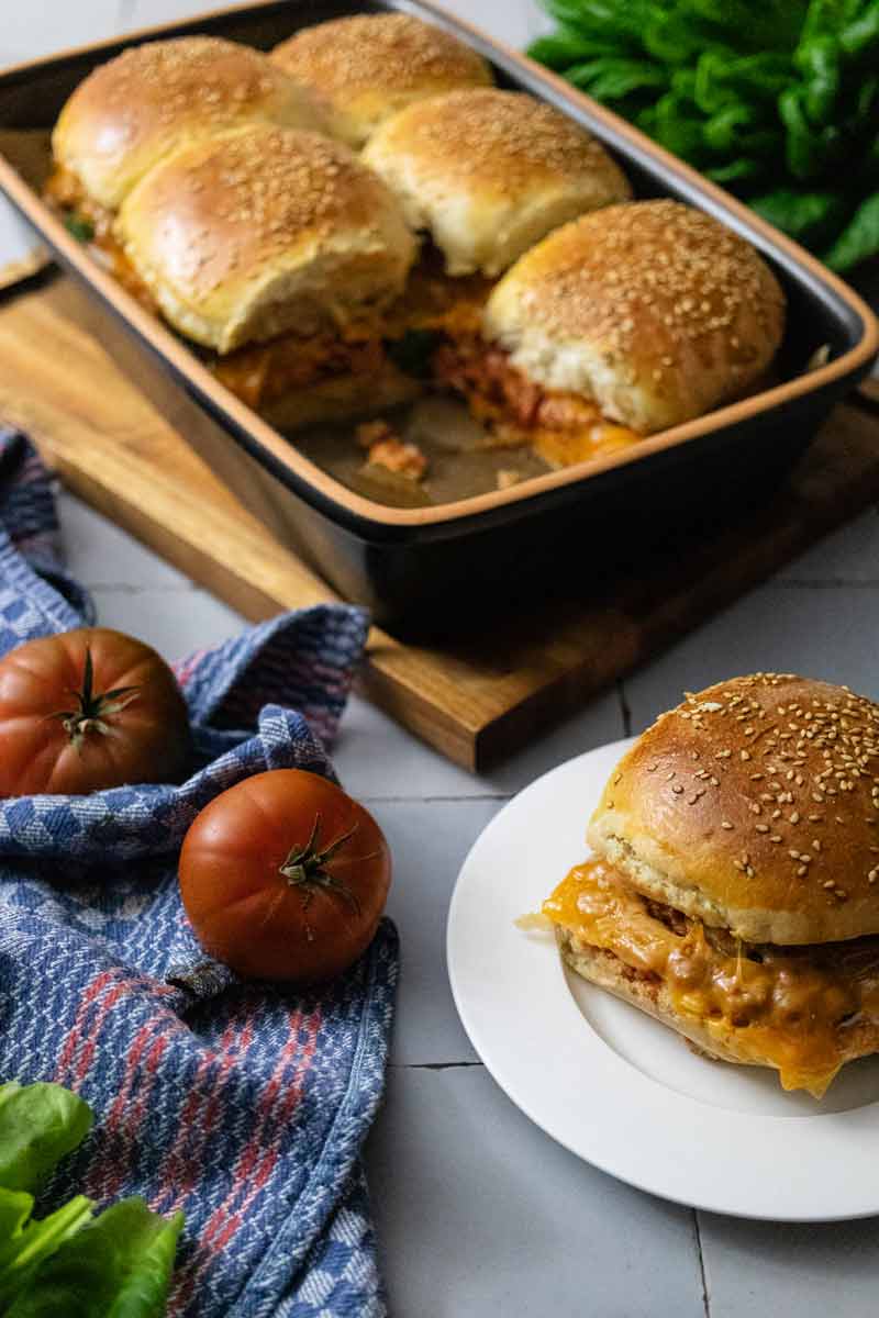 Frische Brötchen mit Käsefüllung in einer Schale, daneben Tomaten und ein einzelnes Brötchen auf einem Teller.