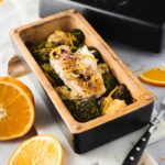 Gebratener Fisch auf Brokkoli und Blumenkohl in einer Form, dekoriert mit Orangenzesten, daneben Orangenscheiben.