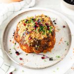 Gebackener Blumenkohl mit Kruste aus Kräutern und Granatapfelkernen auf einem Teller, daneben ein halbierter Granatapfel.