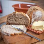 Scheiben hausgemachtes Brot mit Butter auf einem Holzbrett, daneben liegt ein Buttermesser.
