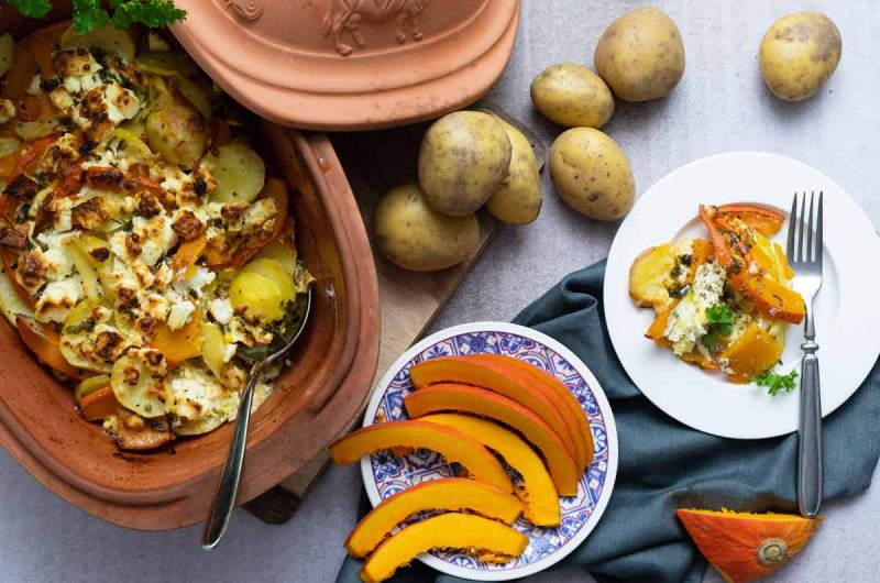 Ton-Topf mit überbackenem Kartoffel-Kürbis-Auflauf, daneben Kartoffeln, Kürbisscheiben und eine Portion auf Teller.