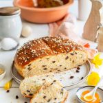 Rosinenbrot auf einem Teller, dekoriert mit Hagelzucker, umgeben von Frühlingsdekorationen wie Narzissen und einem Keramikei.